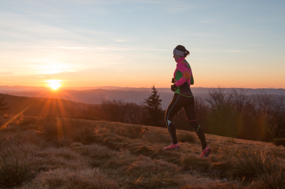 Žena trči po visoravni dok je zalazak Sunca.
