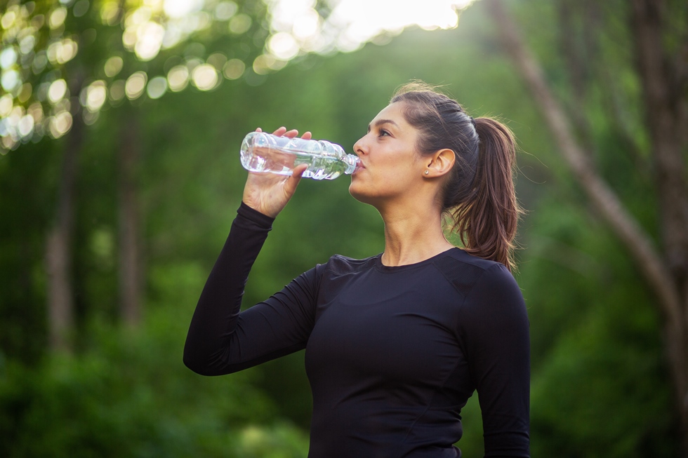 Žena pije vodu dok je u prirodi.