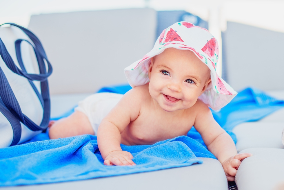 Beba s kapicom leži na trbuhu na plavom ručniku dok se smije.