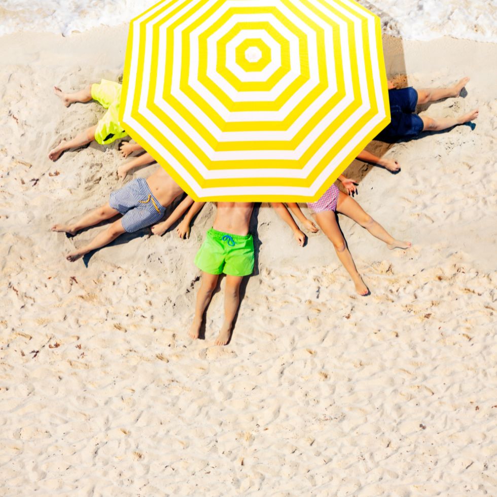 Osobe leže na pješćanoj plaži ispod suncobrana.