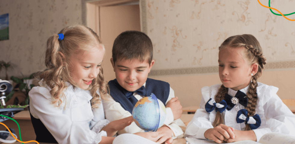 Djeca đačke dobi sjede za stolom dok gledaju globus.