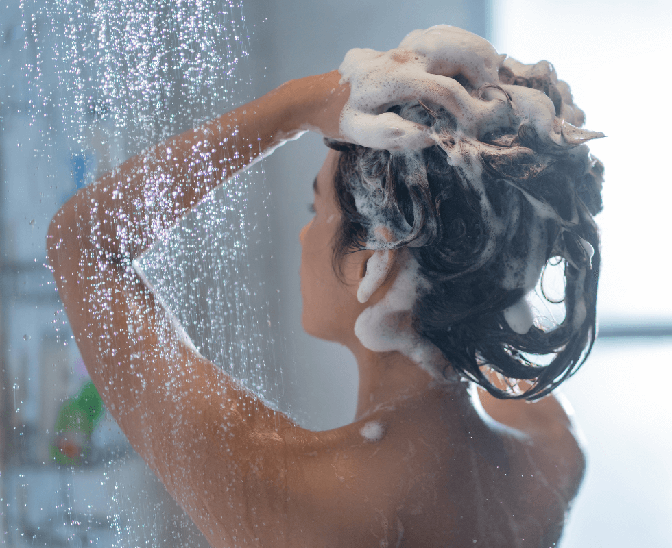 Žena pere kosu u tušu dok teće voda.
