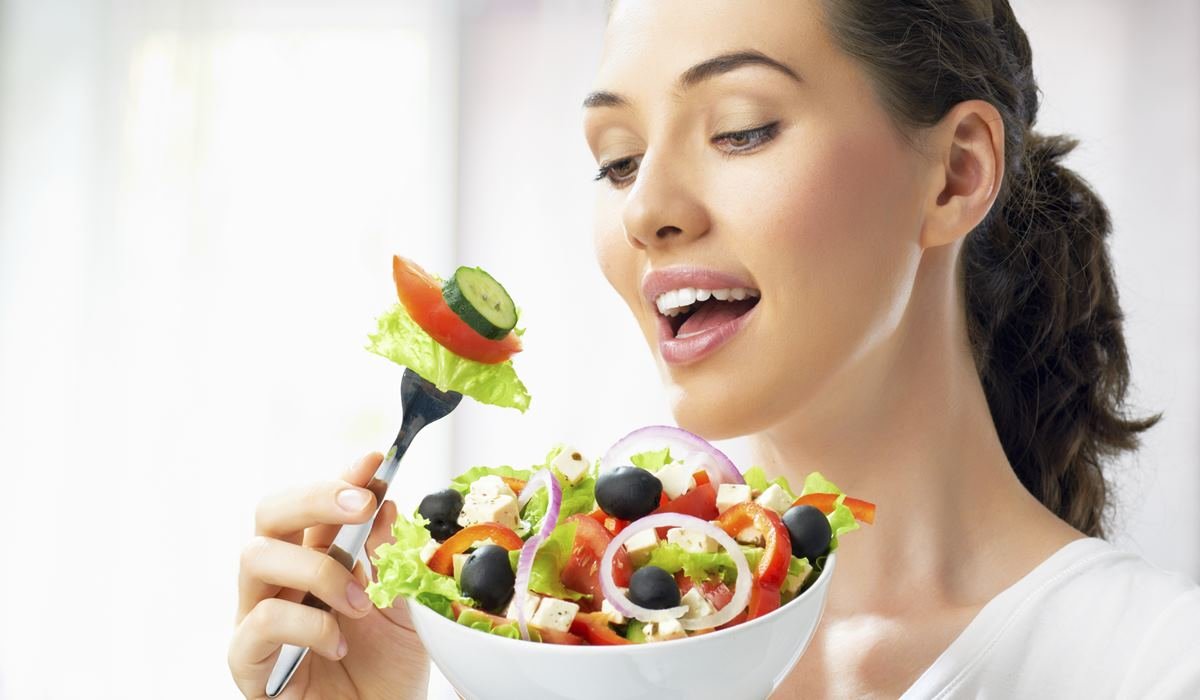 Žena se smije dok jede salatu.
