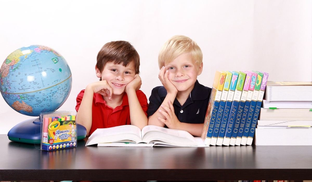 Dva dječaka sjede za radnim stolom pokraj knjiga i globusa.