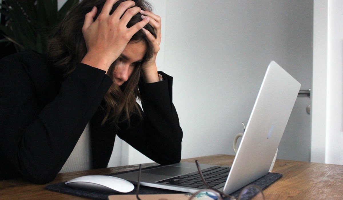 Žena se drži za glavu dok je pred laptopom.