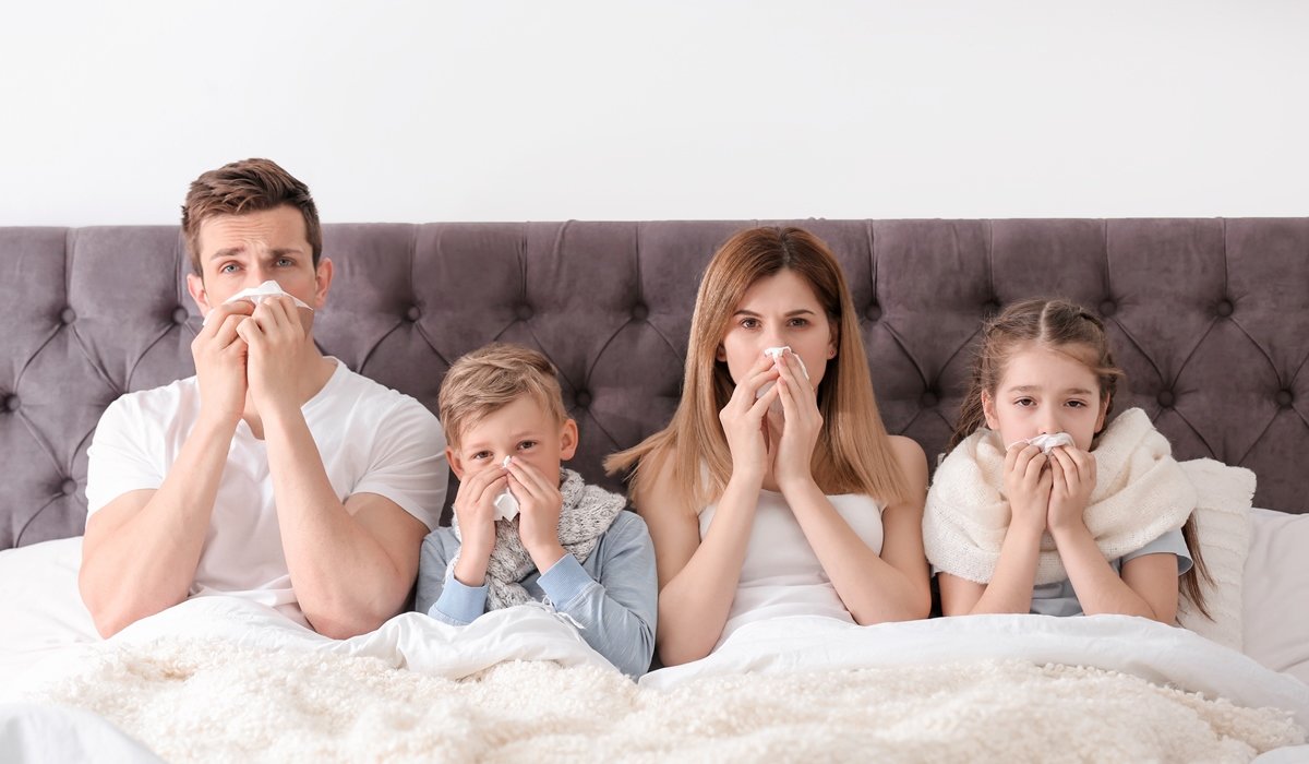 Mama, tata i djeca leže u krevetu dok pušu nos