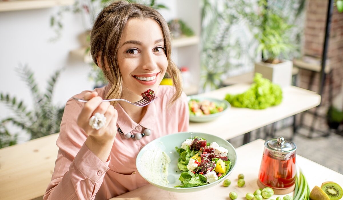 Žena se smije za kuhinjskim stolom dok jede salatu.
